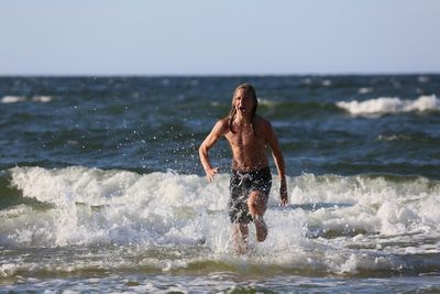 Full length of shirtless man running at beach against clear sky