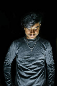 Portrait of young man standing against black background