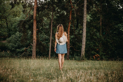 Rear view of woman walking on grassy field in forest