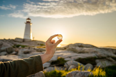 Person holding marble against sky during sunset