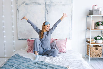 Rear view of woman with arms raised on bed at home