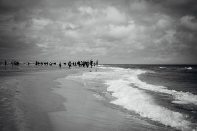 People enjoying at beach against cloudy sky