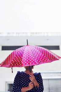 Midsection of woman holding umbrella against sky during rainy season