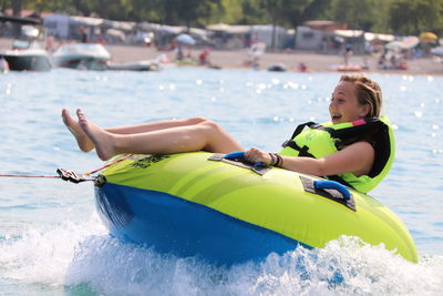 Cheerful teenage girl sitting on inflatable ring in sea