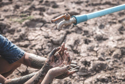 Cropped dirty hands below faucet on barren land during drought