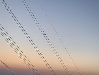 Low angle view of electricity pylon against sky during sunset