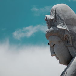 Close-up side view of buddha statue against clouds