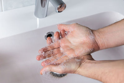 Close-up on a man's hands getting clean with water and soap on a sink.