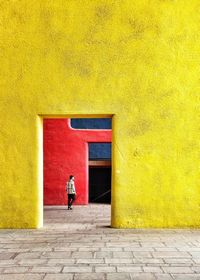 People walking on footpath against yellow wall