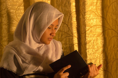 Teenage girl reading book while sitting at home