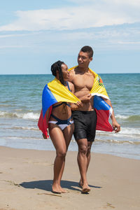 Couple wrapped in a venezuelan flag while walking along the beach together.