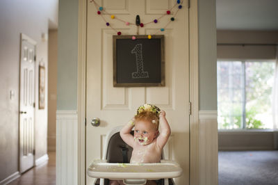 Baby boy playing with cake while sitting on high chair at home during birthday