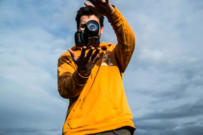 Low angle view of man photographing with camera against sky