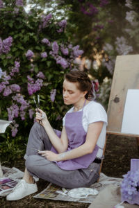 Side view of a smiling young woman holding purple flowering plants