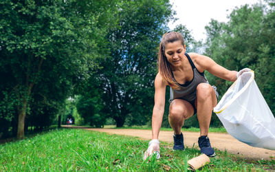 Full length of woman picking up garbage on grass against trees