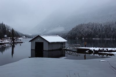 Boathouse by lake against sky during winter