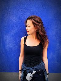 Portrait of young woman standing against blue wall