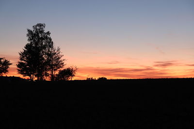 Silhouette trees on field against orange sky