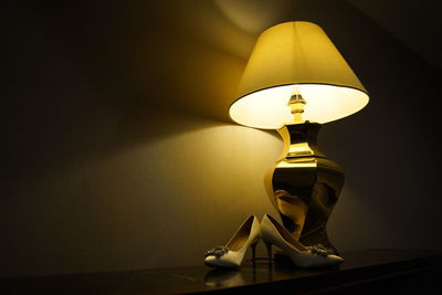 Close-up of illuminated lamp on table against wall at home