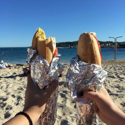 Cropped hands holding sandwiches on beach