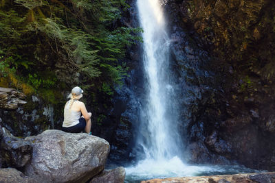 Rear view of woman sitting on rock in forest