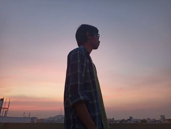 Side view of young man looking away against sky during sunset