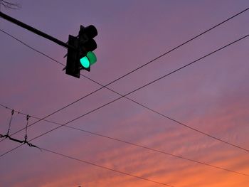 Low angle view of illuminated stoplight against sky during sunset