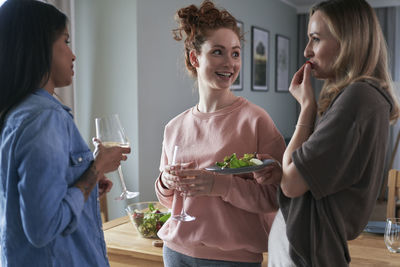 Side view of friends using smart phone while standing at home