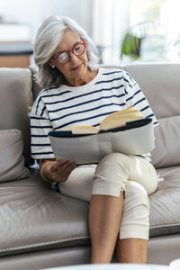 Woman reading book sitting with legs crossed on sofa at home