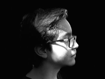 Profile view of teenage boy wearing eyeglasses against black background