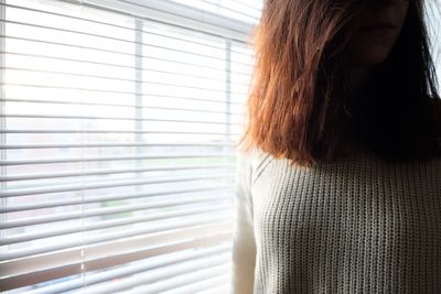 Midsection of mid adult woman standing by window at home