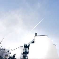 Low angle view of vapor trail over buildings against sky