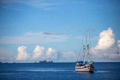 Ship sailing in blue sea against cloudy sky