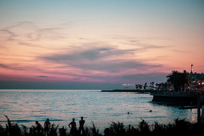 Silhouette people at beach against sky during sunset