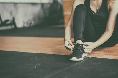 Low section of woman tying shoelace on floor at home