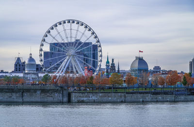 Ferris wheel by river against sky in city