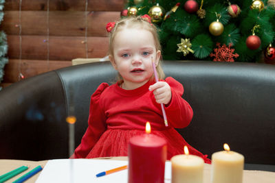 A sad, tearful three year old girl red dress with a pencil in her hand against 