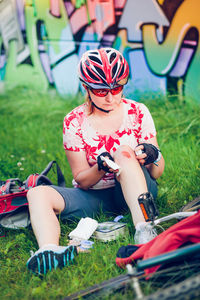 Injured female cyclist applying medicine on wound while sitting at park