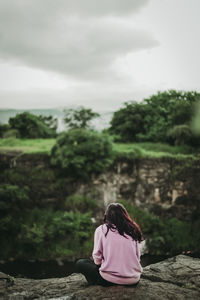 Rear view of woman sitting on rock against sky