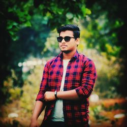 Young man wearing sunglasses standing against trees