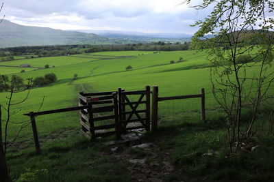 Scenic landscape view of gate leading to fields, against cloudy sky and hill mountain