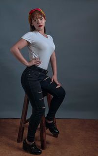 Portrait of young woman sitting on table against wall