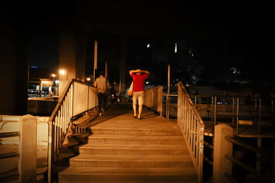 Rear view of woman standing on railing at night