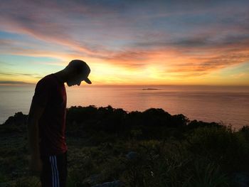 Silhouette man looking at sea against sky during sunset