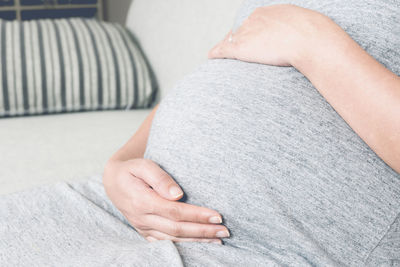 Midsection of pregnant woman sitting on sofa at home