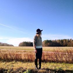 Woman in hat standing on field against blue sky during sunny day