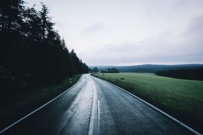 Road by grassy field against sky