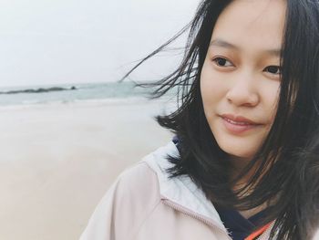 Close-up portrait of smiling young woman standing at beach