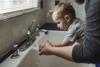 Side view of young boy having hands washed in sink by dad