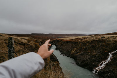 Hand pointing at the canyon with a turquoise river in iceland